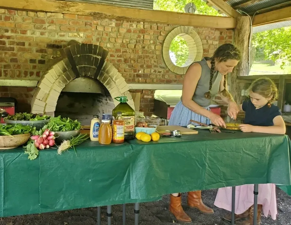 A woman and child preparing food on an outdoor table.