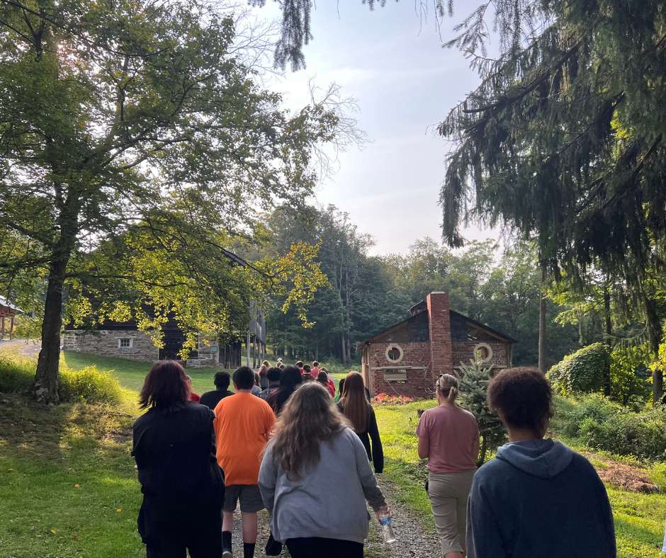 A group of people walking on the grass near trees.