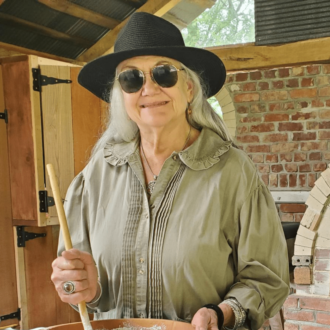 Woman in hat and sunglasses holding a wooden spoon.