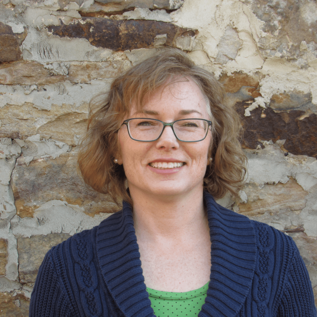 Smiling woman with glasses in front of a stone wall.