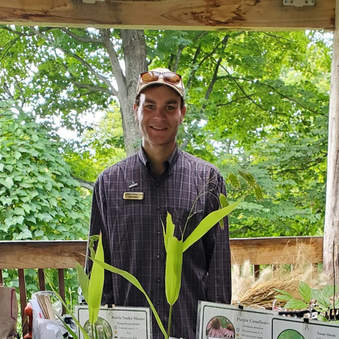 Man in plaid shirt with plants and signs.