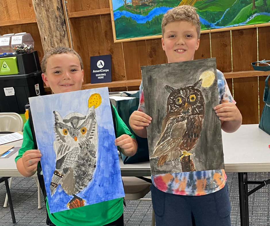 Two boys holding owl paintings.