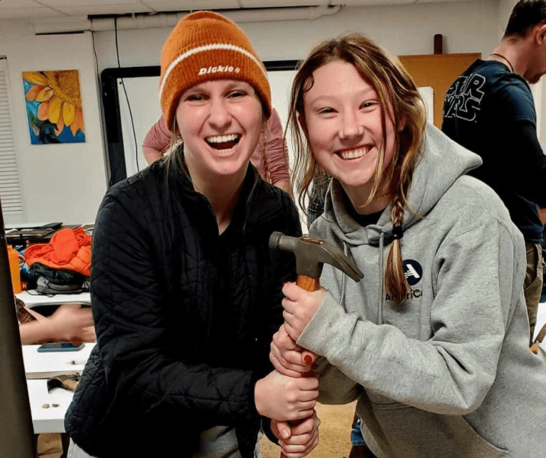 Two Americorp members holding a hammer and smiling for a photo